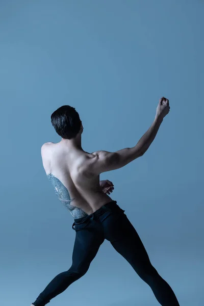 Pohled zezadu na mladého muže, pružného baletního tanečníka, který tančí izolovaně na starém námořnickém pozadí. Umění, pohyb, inspirace. — Stock fotografie