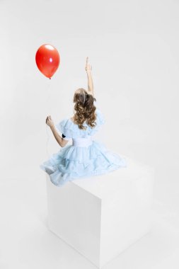 Cadılar Bayramı elbisesi giymiş, yüzünde ürkütücü bir ifade olan genç bir kızın büyük bir kutunun üzerinde oturması.