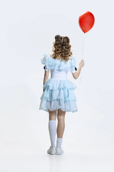 Wstecz widok młodej dziewczyny w sukience Halloween, kostium postaci filmowej stojącej z czerwonym balonem w ręku odizolowany na niebieskim tle — Zdjęcie stockowe
