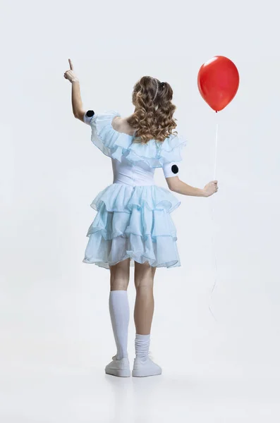 年轻女孩穿着万圣节礼服，穿着电影角色的服装，手拿着红色气球站在蓝色背景下的背影 — 图库照片