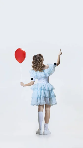 Bakåt syn på ung flicka bär Halloween klänning, kostym av filmkaraktär står med röd ballong i handen isolerad över blå bakgrund — Stockfoto