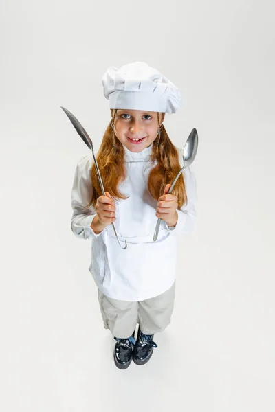 Vista de ángulo alto de la niña linda en uniforme de cocinero blanco y enorme chefs sombrero posando aislado sobre fondo de estudio blanco. — Foto de Stock