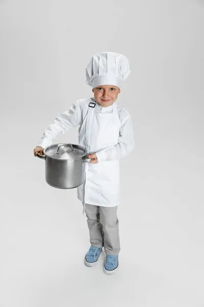 Muotokuva pieni onnellinen poika valkoinen kokki, kokki takki ja hattu seisoo eristetty valkoinen studio tausta. — kuvapankkivalokuva