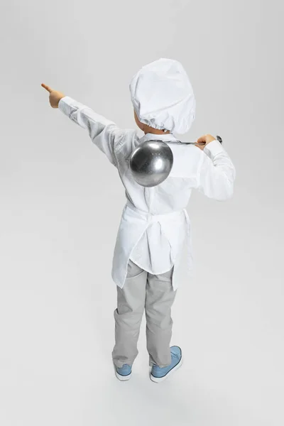 后面是小男孩，身穿白衣的孩子，穿着厨师夹克，戴着帽子，孤立地站在白色的工作室背景下. — 图库照片