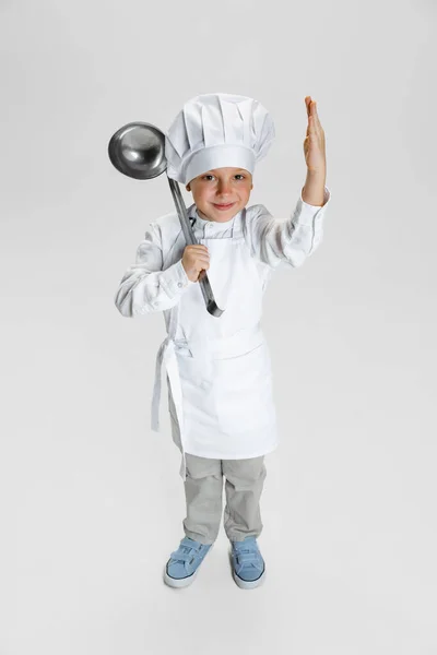 Retrato de menino feliz em cozinheiro branco, jaqueta de chef e chapéu de pé isolado no fundo do estúdio branco. — Fotografia de Stock