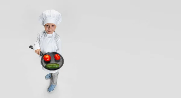 Retrato de niño feliz en cocinero blanco, chaqueta de chef y sombrero de pie con sartén aislado sobre fondo blanco estudio. — Foto de Stock