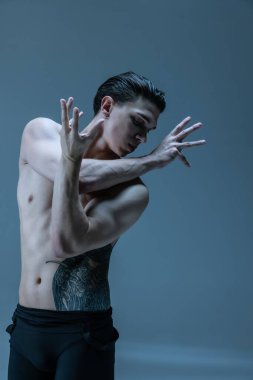 Genç bir adamın yarım boy portresi. Esnek erkek dansçı. Eski donanma stüdyosunun arka planında yalnız dans ediyor. Sanat, hareket, ilham kavramı.