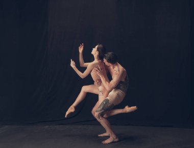 Modern sanat performansında iki esnek dansçı, genç adam ve kadın siyah stüdyo arka planında izole edilmiş. Sanat, hareket, ilham kavramı.