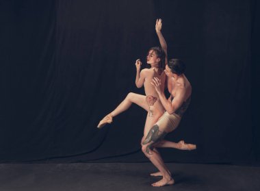 Modern sanat performansında iki esnek dansçı, genç adam ve kadın siyah stüdyo arka planında izole edilmiş. Sanat, hareket, ilham kavramı.