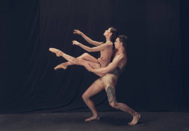 Modern sanat performansında iki esnek dansçı, genç adam ve kadın siyah stüdyo arka planında izole edilmiş. Sanat, hareket, ilham kavramı.