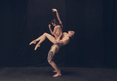 Modern sanat performansında iki esnek dansçı, genç adam ve kadın siyah stüdyo arka planında izole edilmiş. Sanat, hareket, ilham kavramı.