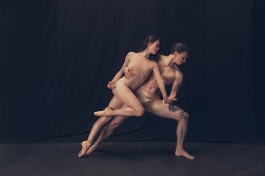 Modern sanat performansında iki esnek dansçı, genç adam ve kadın siyah stüdyo arka planında izole edilmiş. Sanat, hareket, ilham kavramı.
