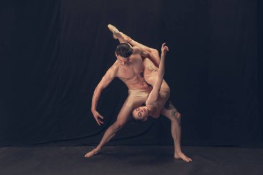 Modern sanat performansında iki esnek dansçı, genç adam ve kadın siyah stüdyo arka planında izole edilmiş. Sanat, hareket, ilham kavramı.