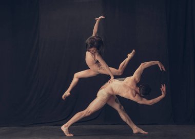 Modern sanat performansında iki esnek dansçı, genç adam ve kadın siyah stüdyo arka planında izole edilmiş. Sanat, hareket, ilham kavramı.