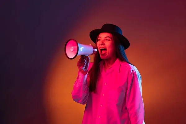 Emocionální mladá dívka křičí na megafon izolované na tmavém pozadí studia v neonovém světle. — Stock fotografie