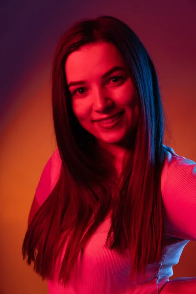 Menina feliz encantadora isolado no fundo do estúdio escuro em luz de néon. Conceito de emoções humanas, expressão facial — Fotografia de Stock
