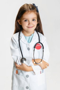 Yakından güzel, küçük bir kız, beyaz laboratuvar önlüğü giymiş, beyaz stüdyo arka planında izole poz veren bir çocuk.