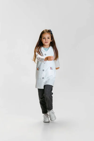 Full-délka portrét roztomilé krásné holčičky, dítě v obraze lékaře na sobě bílý laboratorní plášť chůze izolované na bílém pozadí studia — Stock fotografie