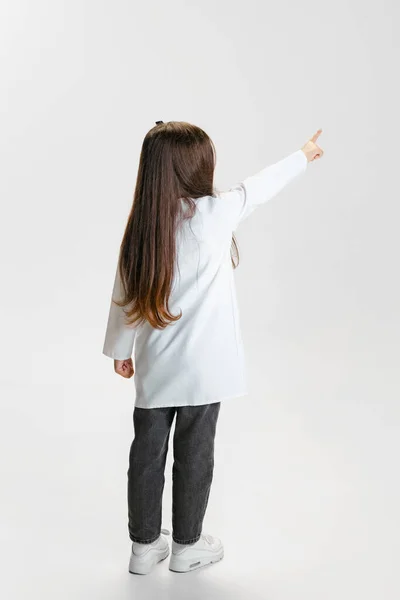 Zadní pohled. Roztomilá krásná holčička, dítě v obrazu lékaře na sobě bílé laboratorní plášť pózovat izolované na bílém pozadí studia — Stock fotografie