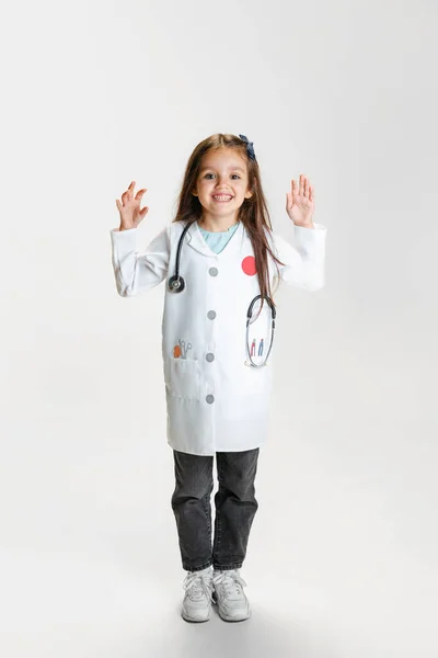 Πλήρες πορτρέτο του χαριτωμένο όμορφο κοριτσάκι, παιδί κατ 'εικόνα του γιατρού φορώντας λευκή ρόμπα εργαστηρίου θέτουν απομονωμένο σε λευκό φόντο στούντιο — Φωτογραφία Αρχείου