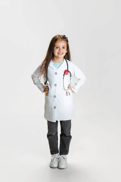 学龄前美女，身穿白色实验室外套的医生形象中的孩子，在白色工作室背景下显得孤立无援 — 图库照片
