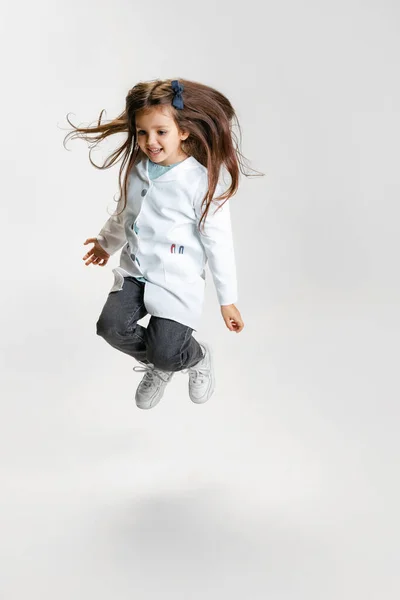Retrato completo de bonito menina bonita, criança na imagem de médico vestindo jaleco branco pulando isolado no fundo do estúdio branco — Fotografia de Stock