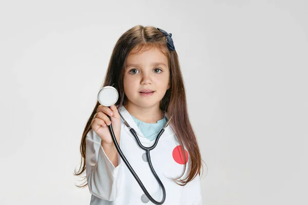 Close-up retrato de menina bonito, criança na imagem de médico vestindo jaleco branco com estetoscópio isolado no fundo do estúdio branco — Fotografia de Stock