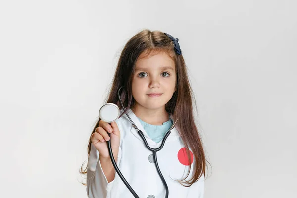 可爱小女孩的特写，身穿白色实验室外套的医生形象中的儿童，在白色工作室背景下与听诊器隔离 — 图库照片