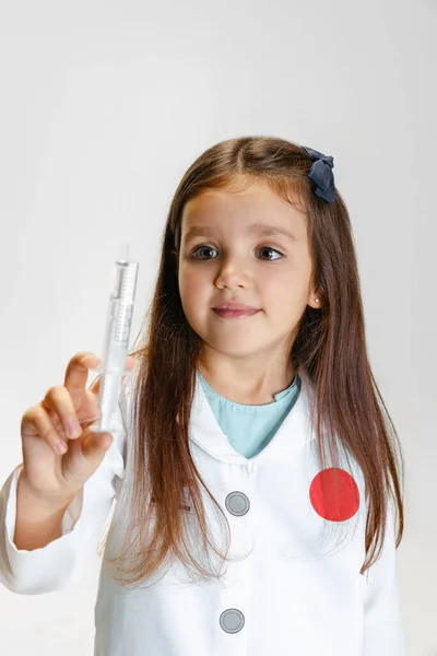 Portret van een schattig mooi meisje, kind in beeld van een arts in witte labjas met speelgoedspuit geïsoleerd op witte studioachtergrond — Stockfoto