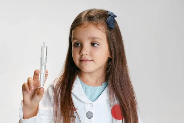 Porträt von niedlichen schönen Mädchen, Kind in Bild des Arztes trägt weißen Labormantel mit Spielzeugspritze isoliert auf weißem Studiohintergrund — Stockfoto