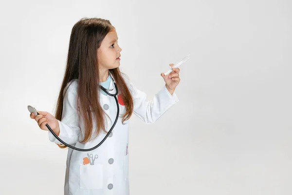 Close-up retrato de menina bonito, criança na imagem de médico vestindo jaleco branco com estetoscópio isolado no fundo do estúdio branco — Fotografia de Stock