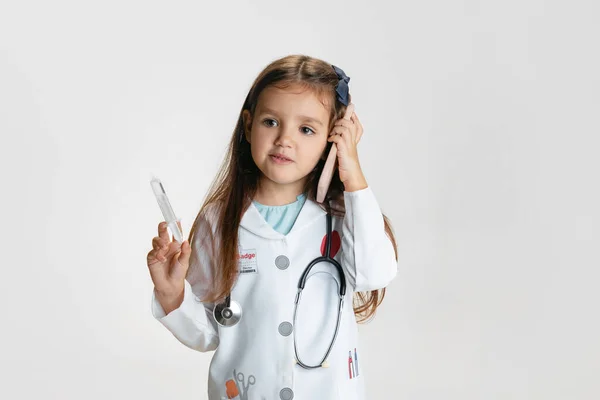 Στούντιο πλάνο του χαριτωμένο κοριτσάκι, παιδί κατ 'εικόνα του γιατρού φορώντας λευκή ρόμπα εργαστηρίου με στηθοσκόπιο απομονώνονται σε λευκό φόντο στούντιο — Φωτογραφία Αρχείου