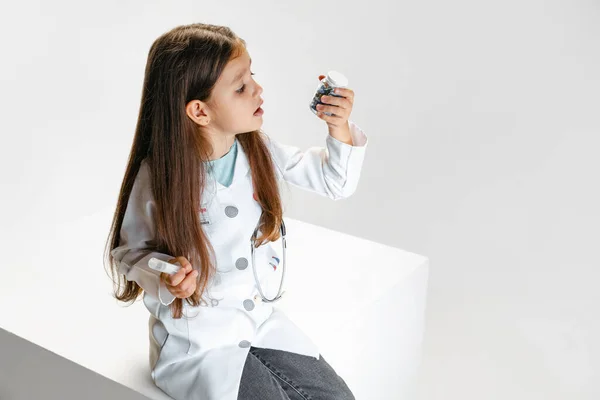 Una bambina carina, bambino a immagine del medico che indossa camice bianco seduto su una scatola enorme isolato su sfondo bianco studio — Foto Stock