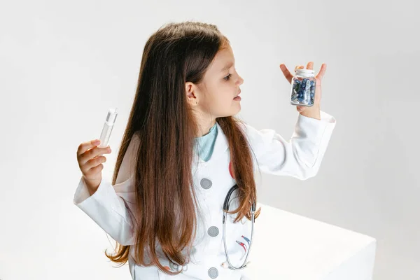 Flyer met schattig klein meisje, kind in beeld van de arts het dragen van witte geneeskunde jas holding pillen geïsoleerd op witte studio achtergrond — Stockfoto