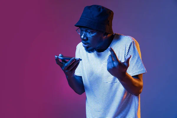 Close-up portret młodego Afrykanina mówiący telefon odizolowany na gradientowym fioletowym tle studio w neonie — Zdjęcie stockowe