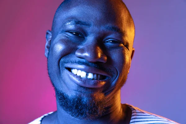 Gros plan portrait d'un jeune Africain souriant regardant une caméra isolée sur fond de studio rose pourpre dégradé au néon — Photo