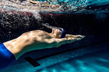 Sualtı çatışması. Bir erkek yüzücü havuzda, kapalı alanda eğitim görüyor. Yüzme hareketlerinin sualtı görüntüsü ayrıntıları.