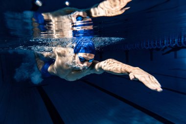 Profesyonel erkek yüzücü yüzme şapkası ve hareket gözlüğü takıyor ve havuz ve kapalı alanda antrenman yaparken hareket ediyor. Sağlıklı yaşam tarzı, güç, enerji, spor hareketi kavramı