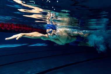 Profesyonel erkek yüzücü yüzme şapkası ve hareket gözlüğü takıyor ve havuz ve kapalı alanda antrenman yaparken hareket ediyor. Sağlıklı yaşam tarzı, güç, enerji, spor hareketi kavramı