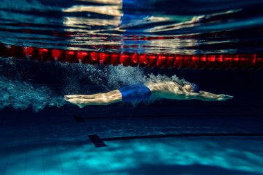 Havuzda, kapalı alanda profesyonel erkek yüzücü eğitimi. Yüzme hareketlerinin sualtı görüntüsü ayrıntıları.