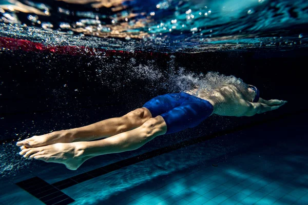 水下射击。一名男子游泳运动员在游泳池训练，在室内。游泳运动的水下景观详情. — 图库照片
