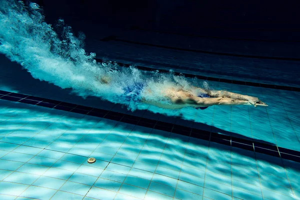 Undervattenskameran fungerar. En manlig simmare tränar vid poolen, inomhus. Undervattensvy över simning detaljer. — Stockfoto