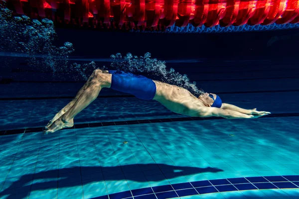 Underwater shooting. One male swimmer training at pool, indoors. Underwater view of swimming movements details.