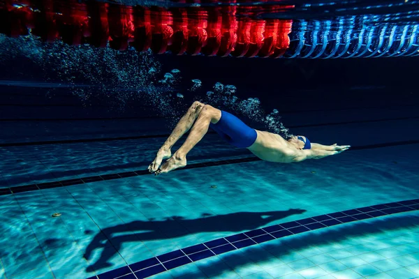 Undervattensskytte. En manlig simmare tränar vid poolen, inomhus. Undervattensvy över simning detaljer. — Stockfoto