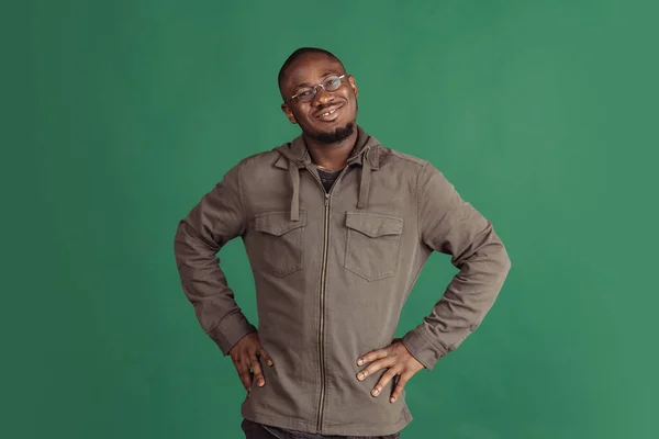 Portrait de jeune homme africain heureux portant des vêtements décontractés isolés sur fond de studio vert foncé. Émotions, concept d'expression faciale. — Photo