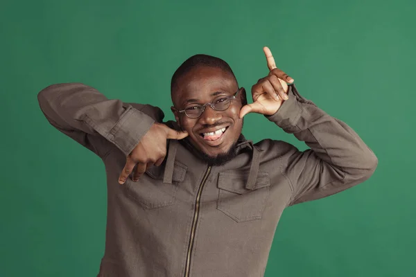 Un jeune homme africain élégant portant des vêtements décontractés isolés sur fond de studio vert foncé. Émotions, concept d'expression faciale. — Photo