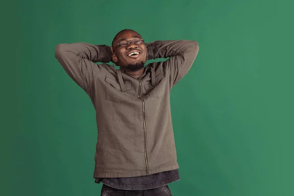 Retrato de jovem homem africano feliz vestindo roupas casuais isolado no fundo do estúdio verde escuro. Emoções, conceito de expressão facial. — Fotografia de Stock