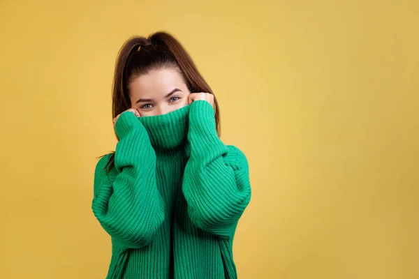 Half-lenght portrait of young cute girl, student wearing green sweater posing isolated on yellow studio background. Concept of emotions, fashion — Stock Photo, Image