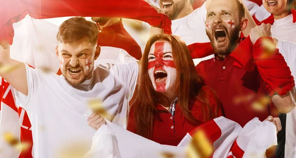 Emocionados por el fútbol, los aficionados al fútbol animan a su equipo con bufandas rojas en los stands del estadio. Concepto de deporte, emociones, evento en equipo, competencia. — Foto de Stock