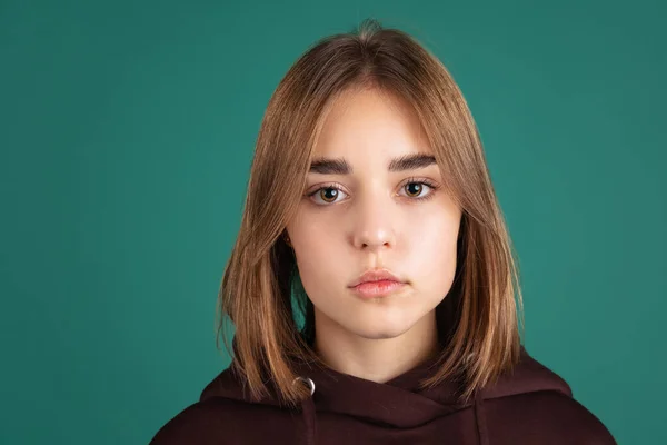 갈색 후드를 입은 학생 이 녹색 빈티지 스튜디오 백합으로 고립된 카메라를 보고 있는 젊은 비올라 소녀의 근접 사진. — 스톡 사진